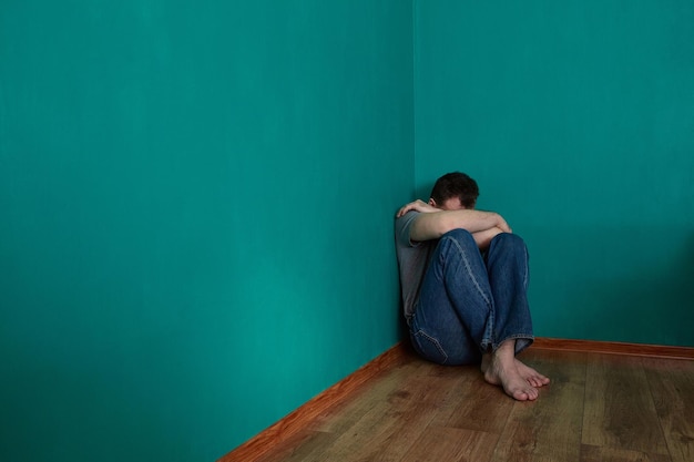 depressed-man-sits-in-a-corner-in-an-empty-green-room-with-his-head-in-his-lap-copy-space_95018-718.jpg